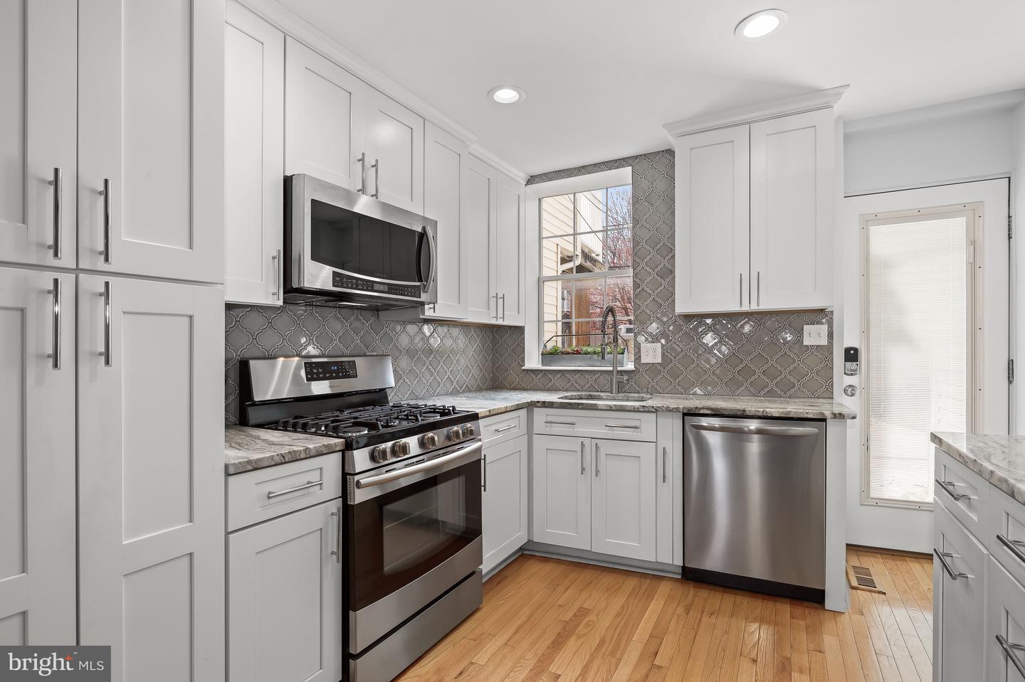 Kitchen with white shaker cabinets, stainless steel appliances, patterned gray backsplash, and hardwood floors.