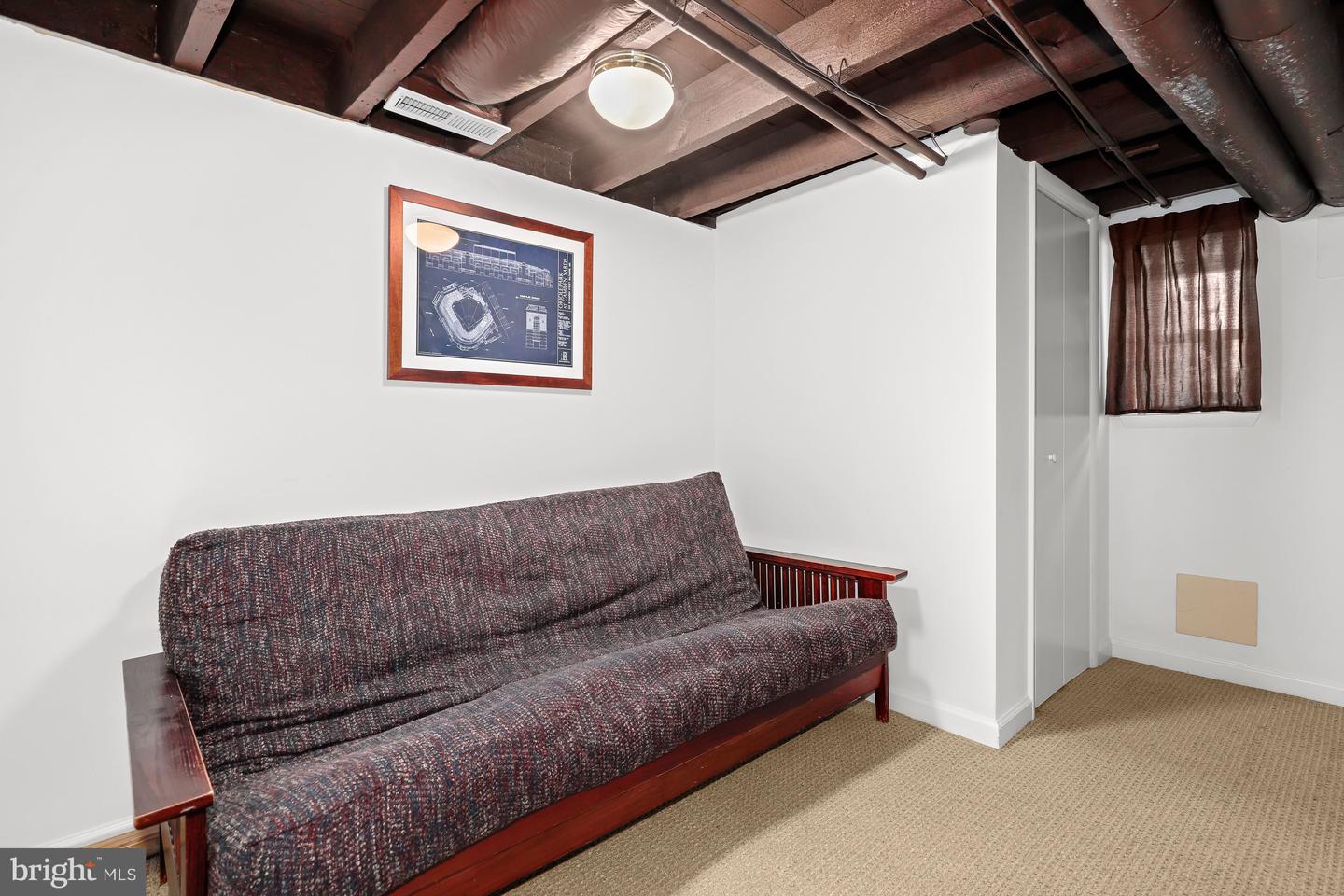 Basement sitting area with a patterned futon beneath exposed ceiling beams.