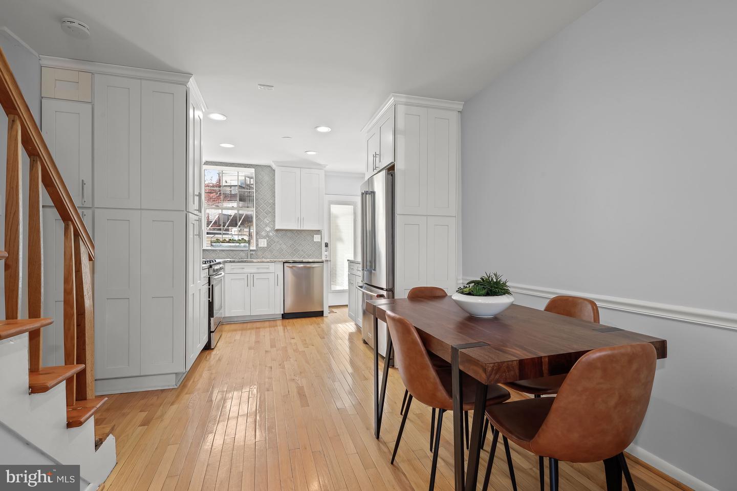 Kitchen and dining area with white cabinets, stainless appliances, hardwood floors, and a dark wood table.