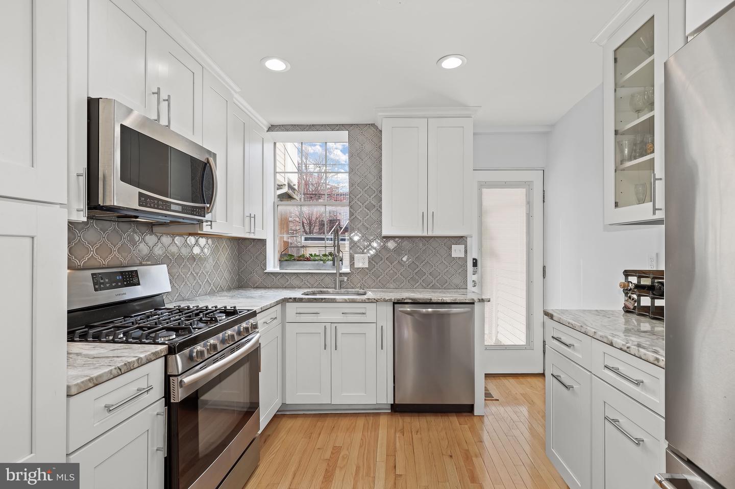 Renovated kitchen with white cabinets, patterned backsplash, stainless appliances, and hardwood floors.