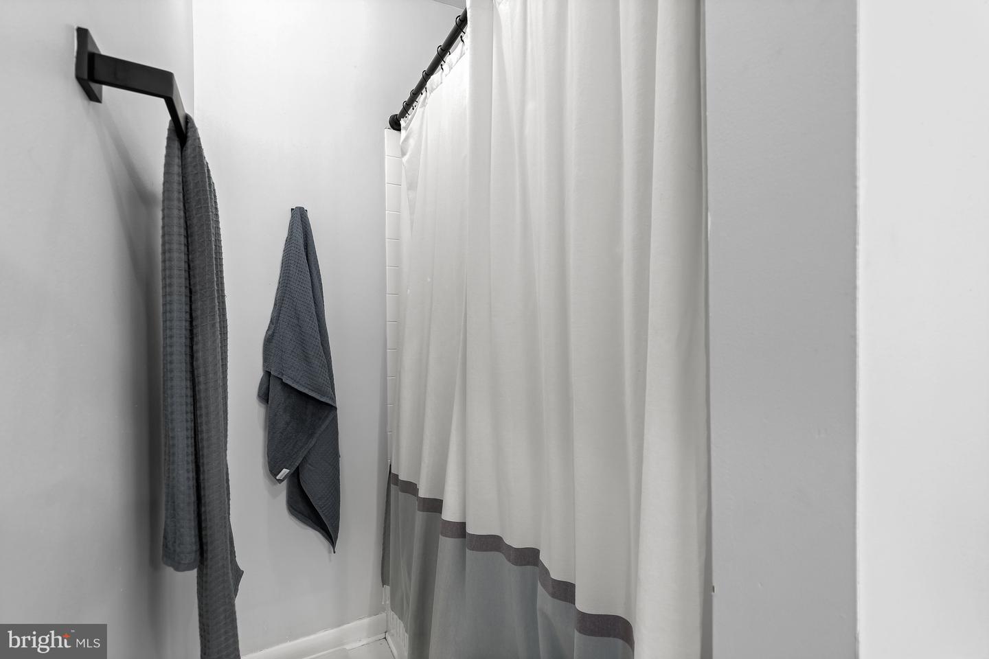 Bathroom shower with a white-and-gray curtain and two dark towels hanging nearby.