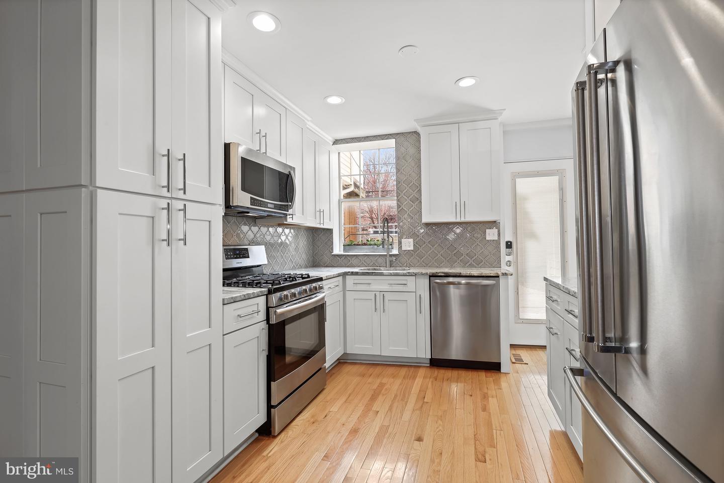 Kitchen with white cabinets, stainless steel appliances, patterned tile backsplash, and hardwood floors.