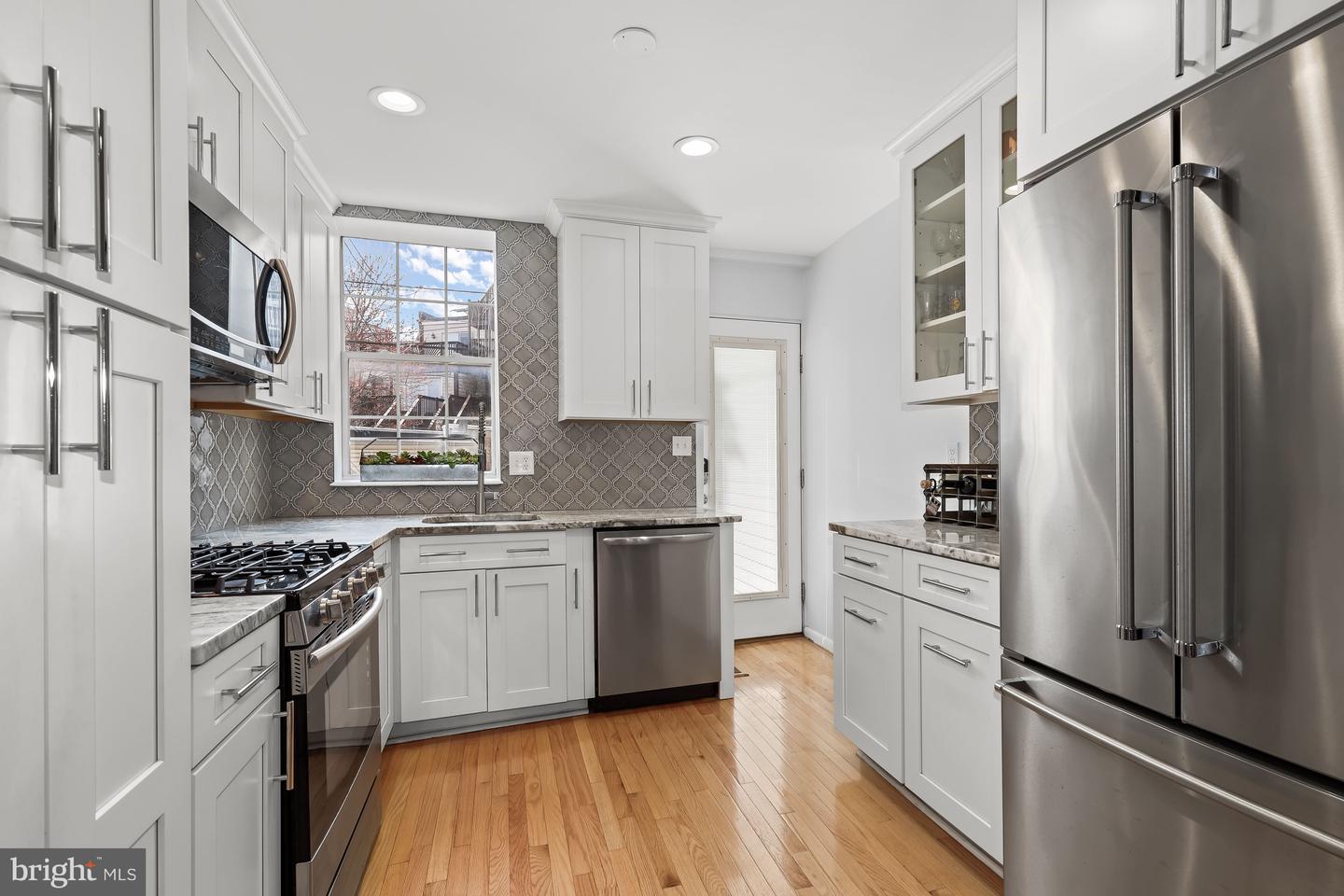 Kitchen with white cabinets, patterned tile backsplash, stainless steel appliances, and warm hardwood floors.