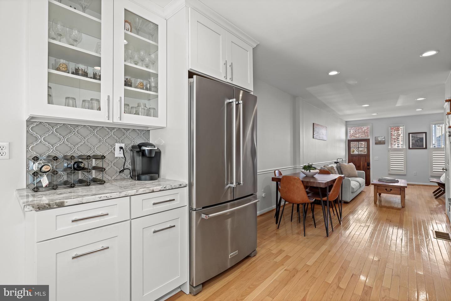Open-plan kitchen with glass-front cabinets and patterned tile backsplash, opening to a dining and living area.