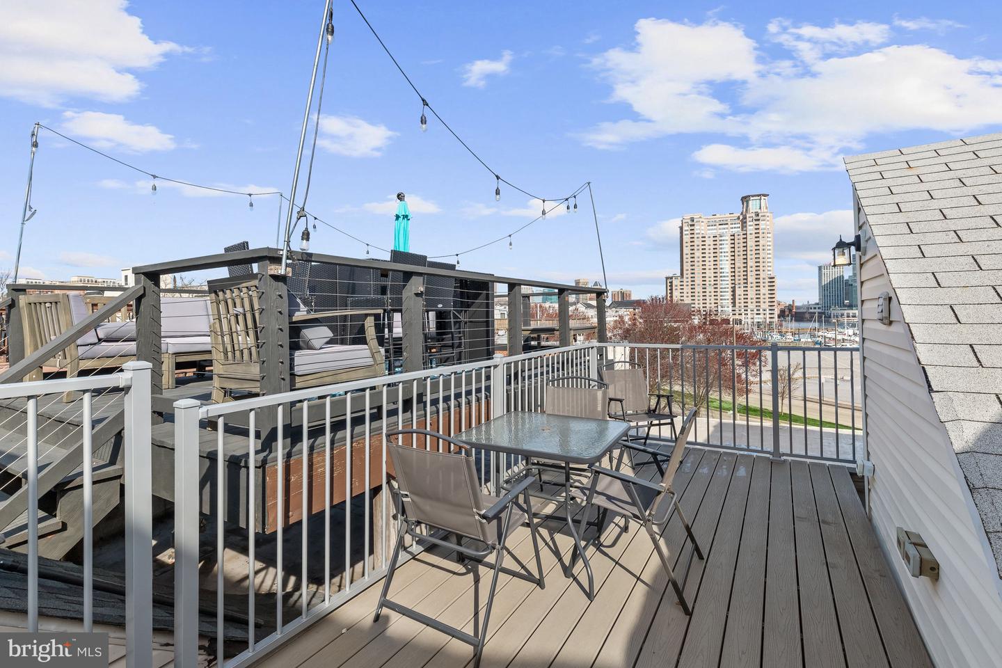 Rooftop deck with outdoor dining furniture, string lights, and Baltimore skyline views.