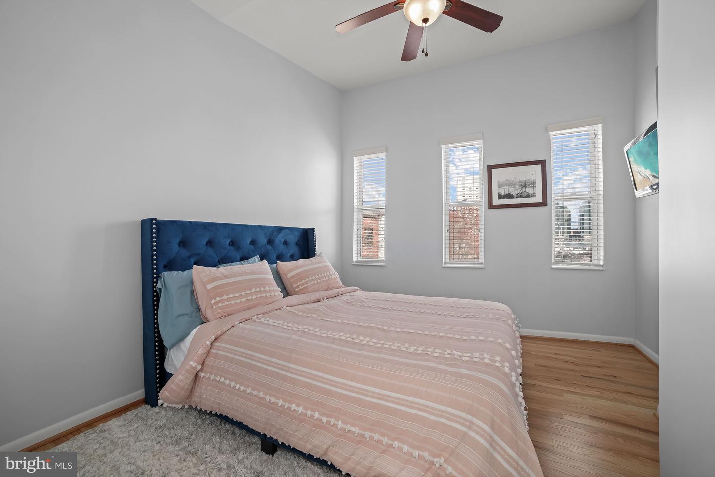 Bedroom with a navy tufted headboard, pink striped bedding, and three tall windows.
