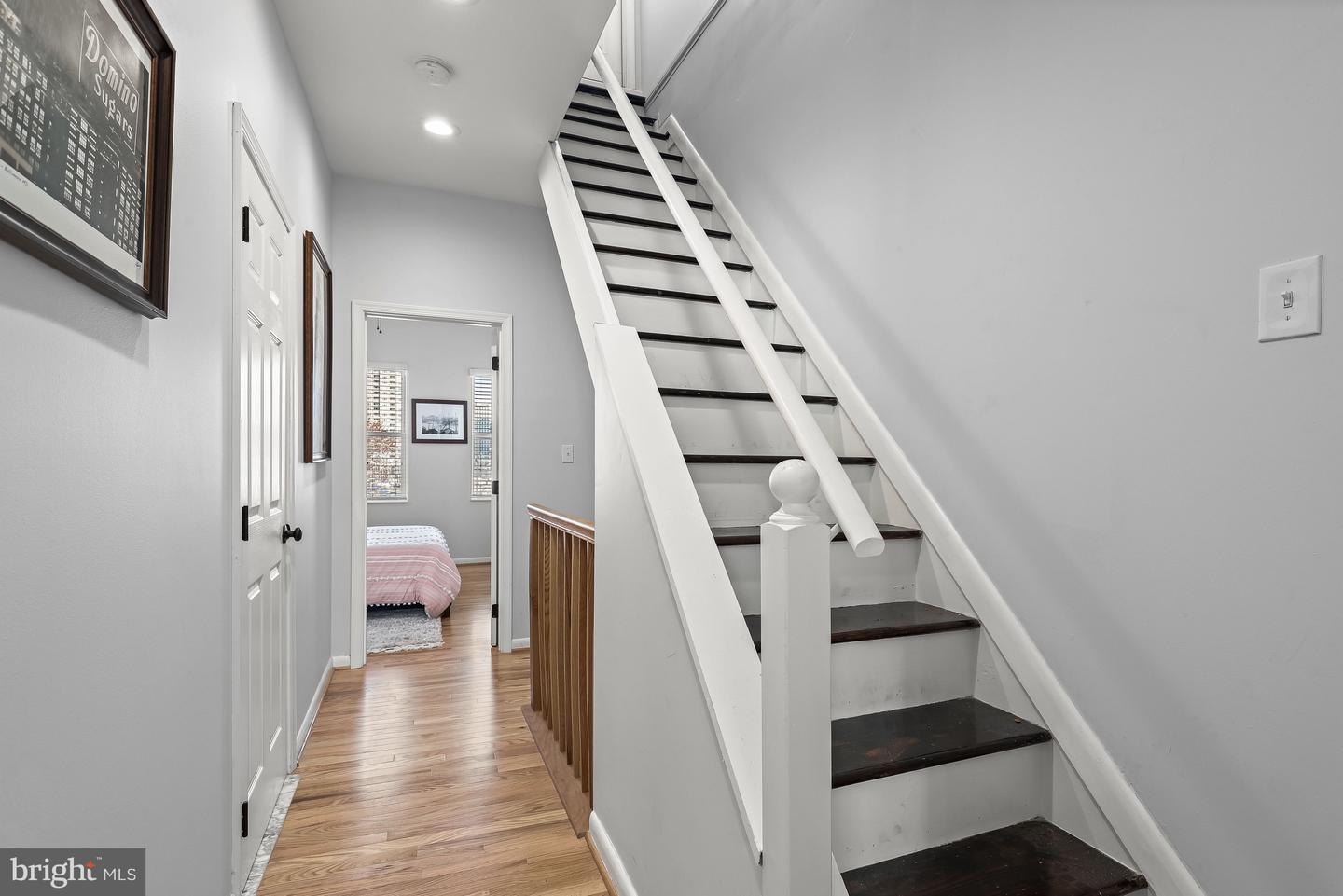 Hallway with a white staircase and dark wood treads, opening onto a bedroom with a pink bedspread.