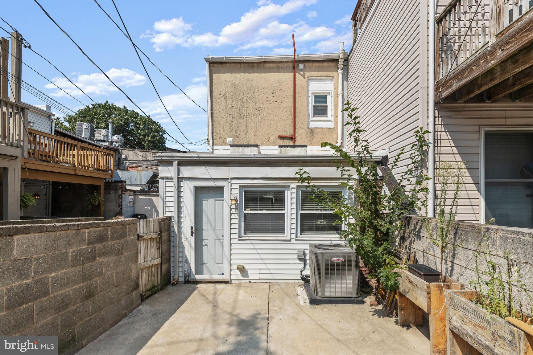 Home’s rear exterior with a concrete patio, raised garden beds, and a fenced courtyard.