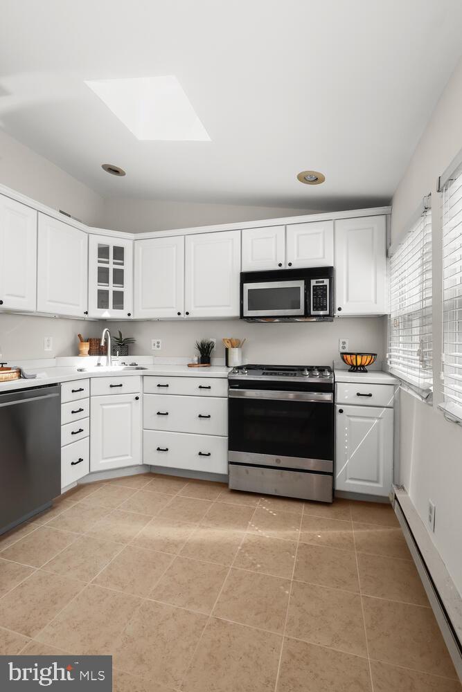 Kitchen with white cabinets, stainless-steel appliances, a gas range, and beige tile flooring.