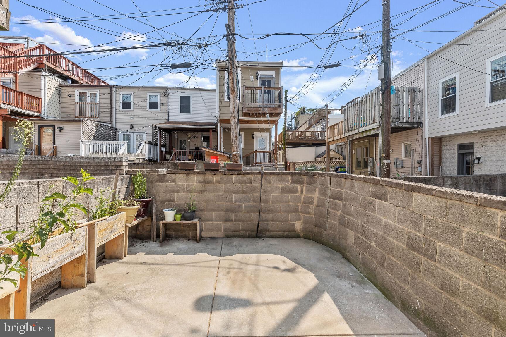 Concrete backyard patio with curved block walls, wooden planter boxes, and potted plants.