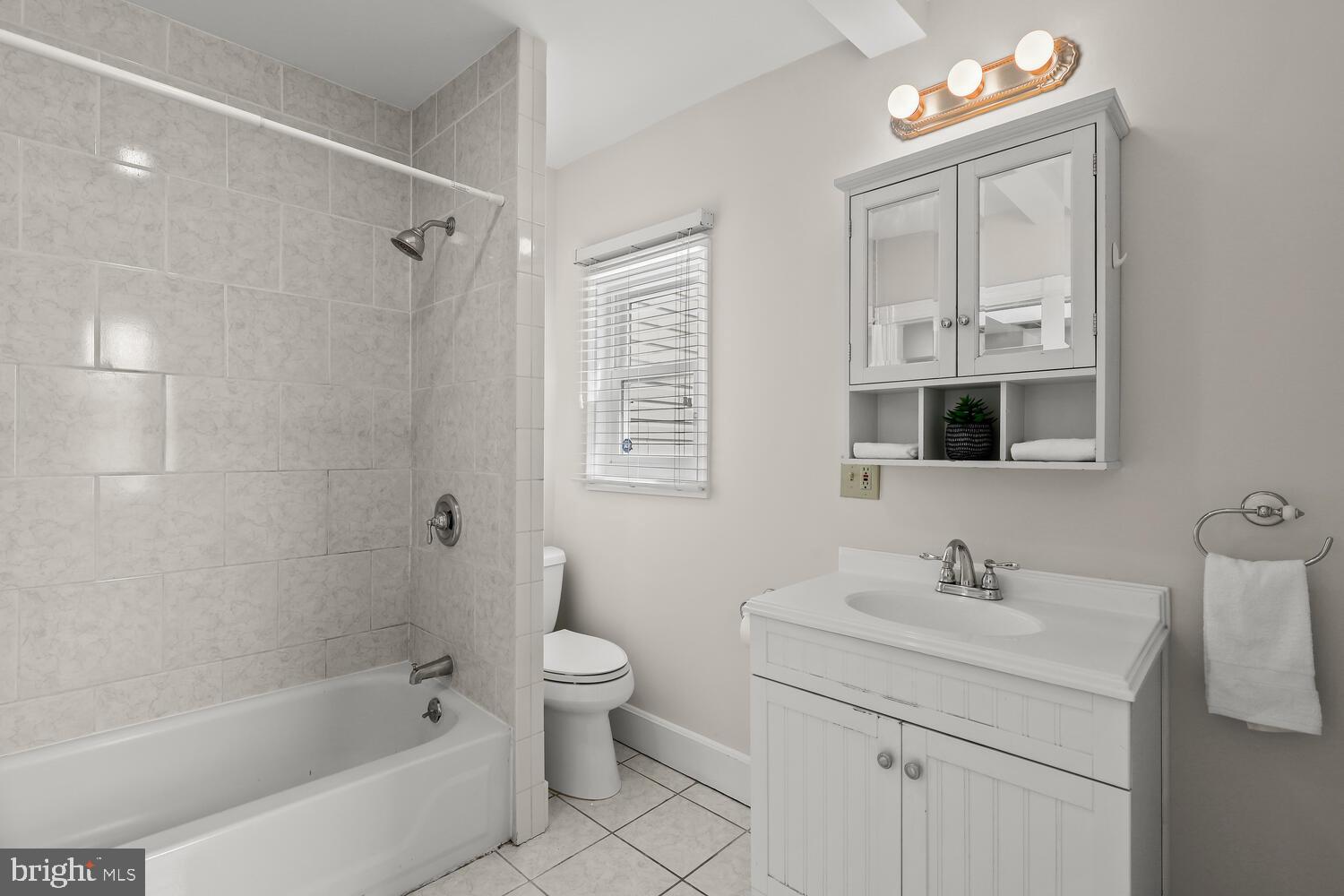 Bathroom with a tiled tub and shower, toilet, and white vanity with mirrored cabinet.