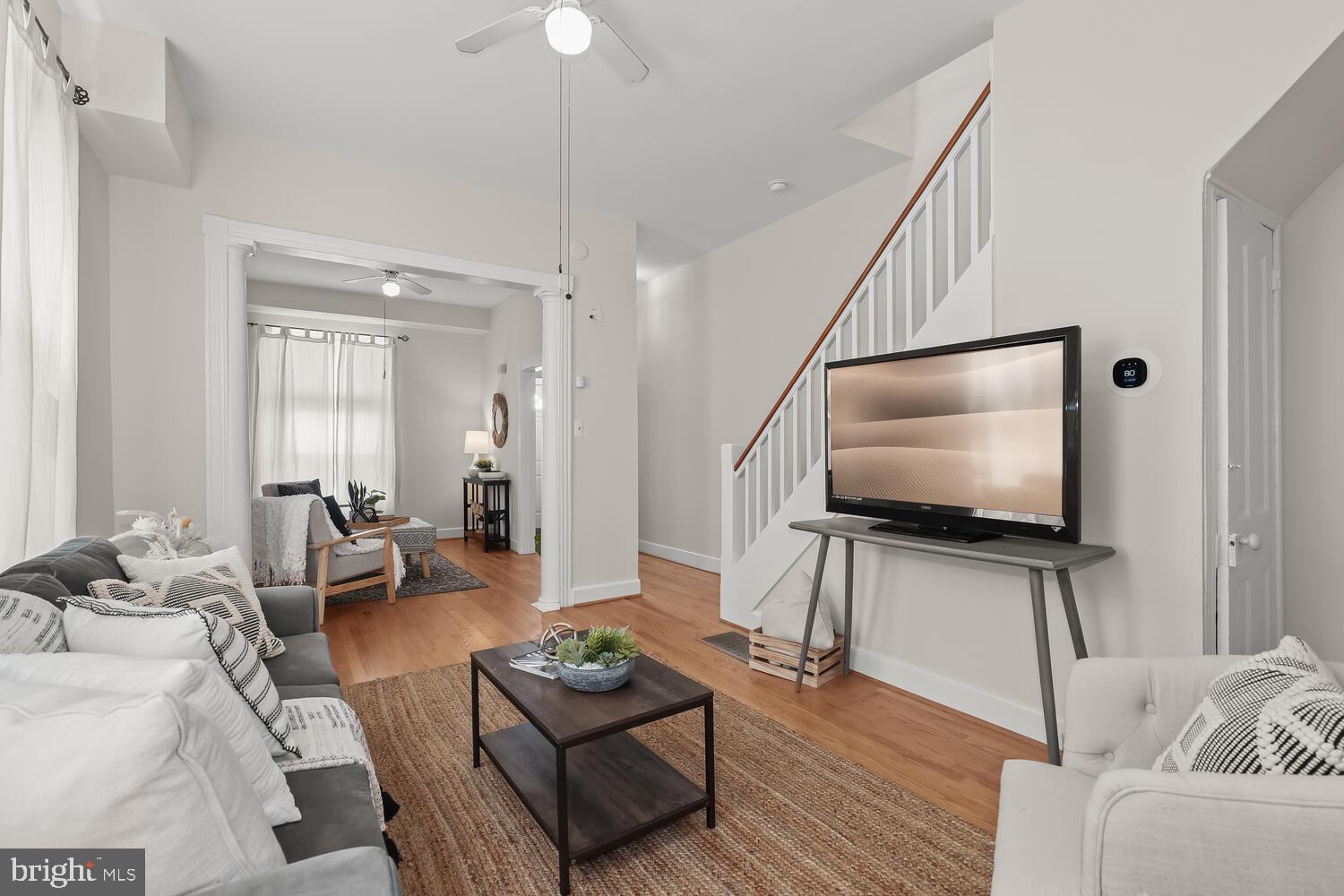 Staged living room with hardwood floors, a staircase, and seating around a coffee table.