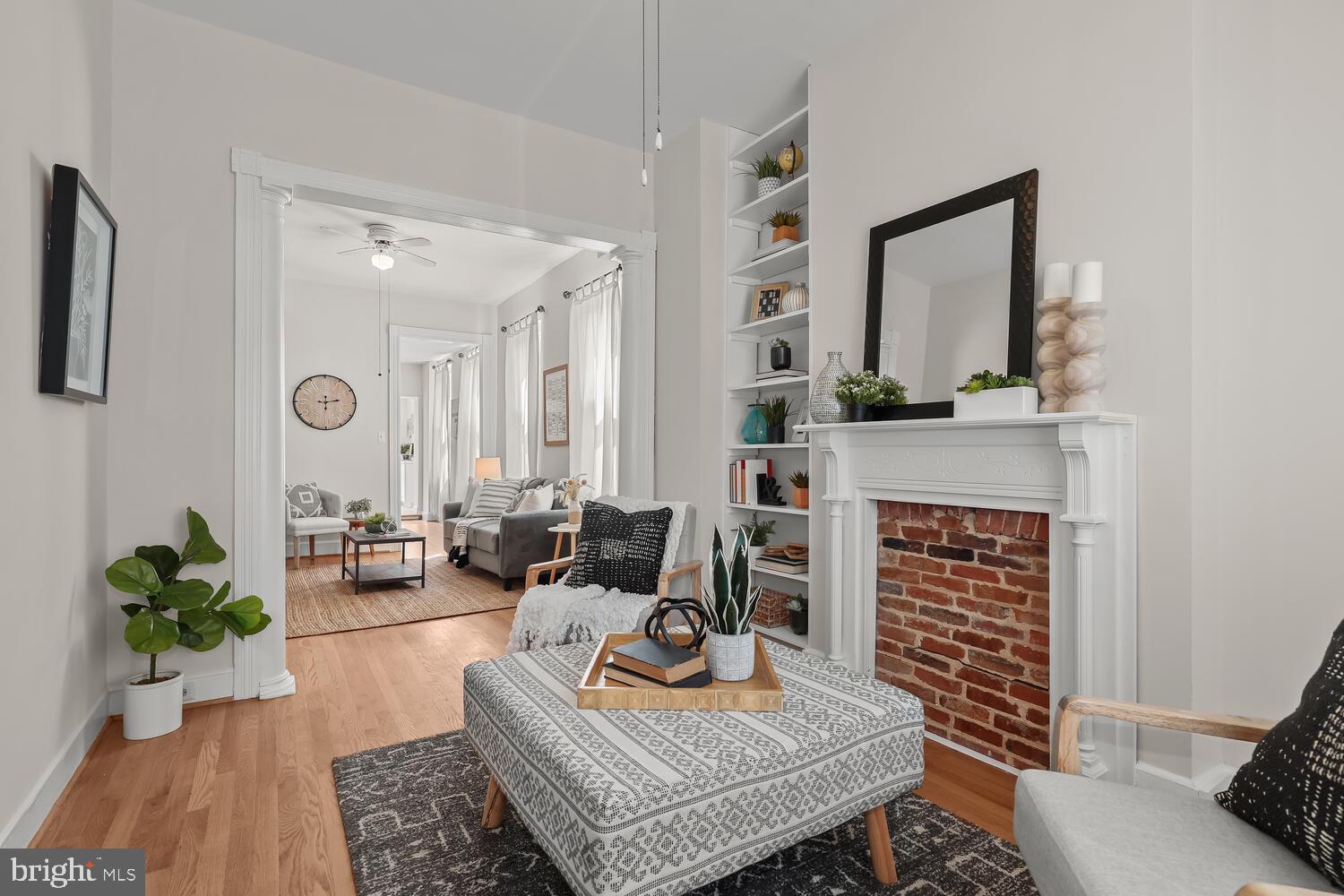 Living room with a white mantel, exposed brick fireplace, built-in shelves, and a view into a second sitting area.