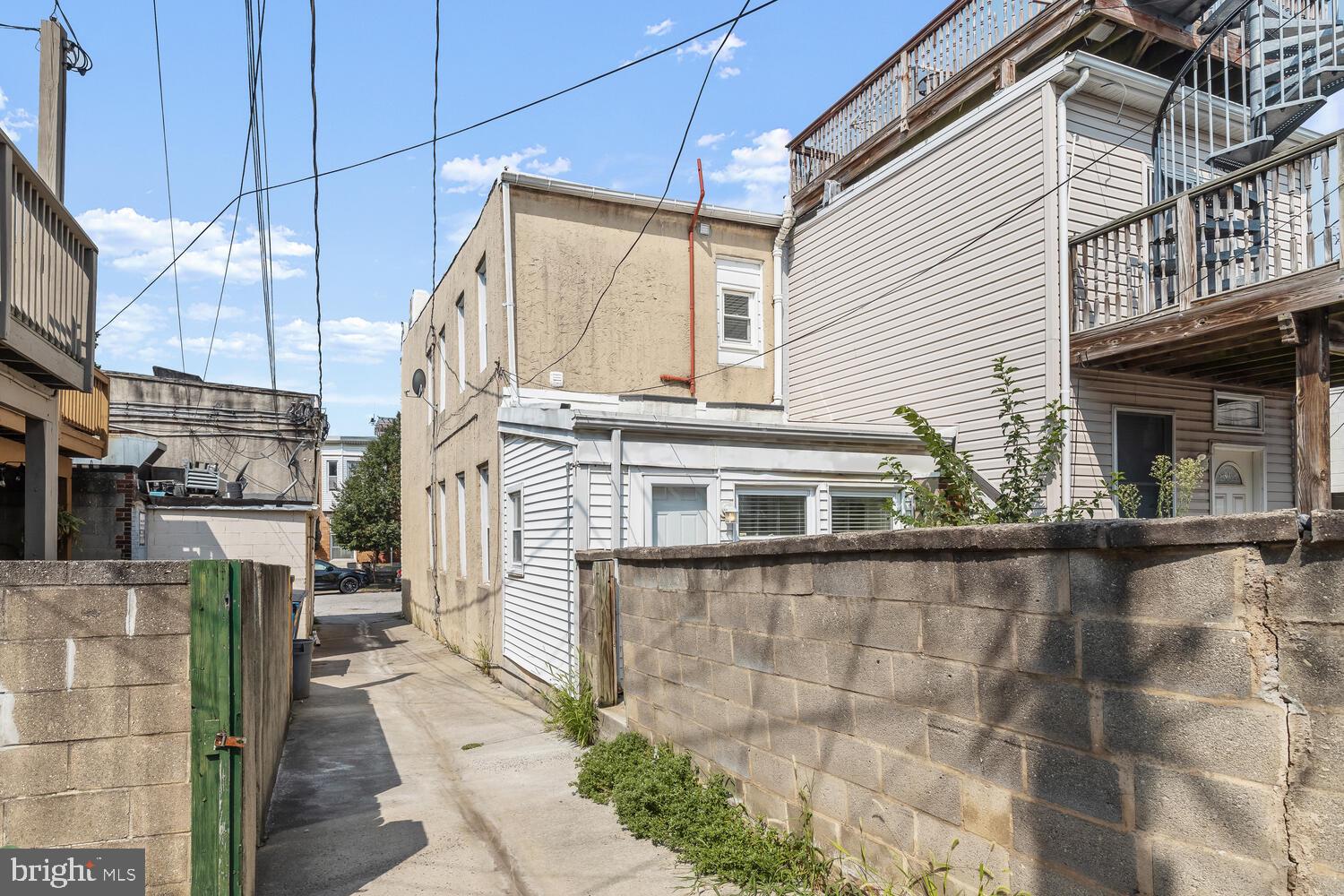 Rear of a Baltimore home beside a narrow concrete alley, with a green gate and neighboring elevated deck.