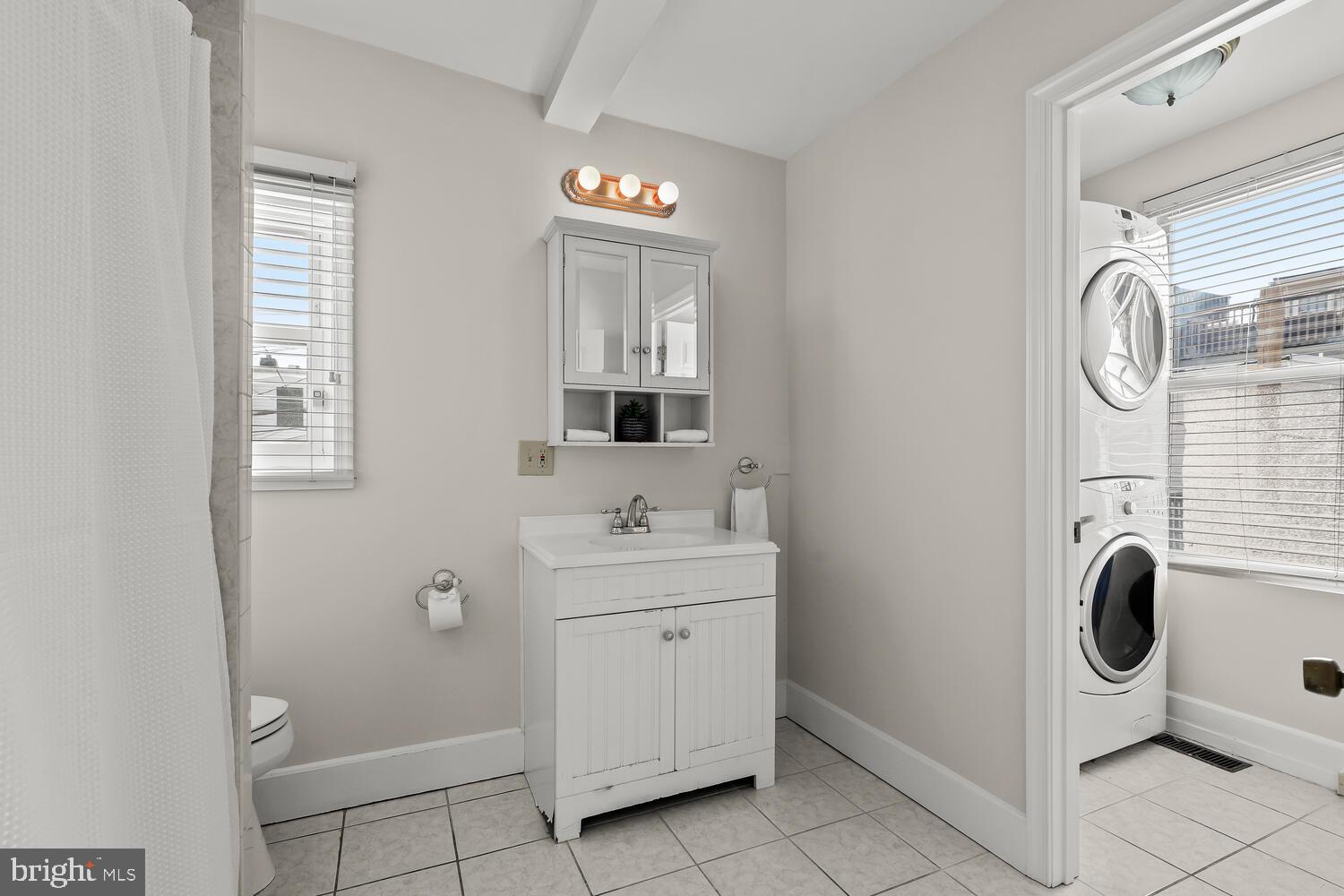Bathroom with a white vanity, tiled floor, and stacked washer and dryer in an adjoining nook.
