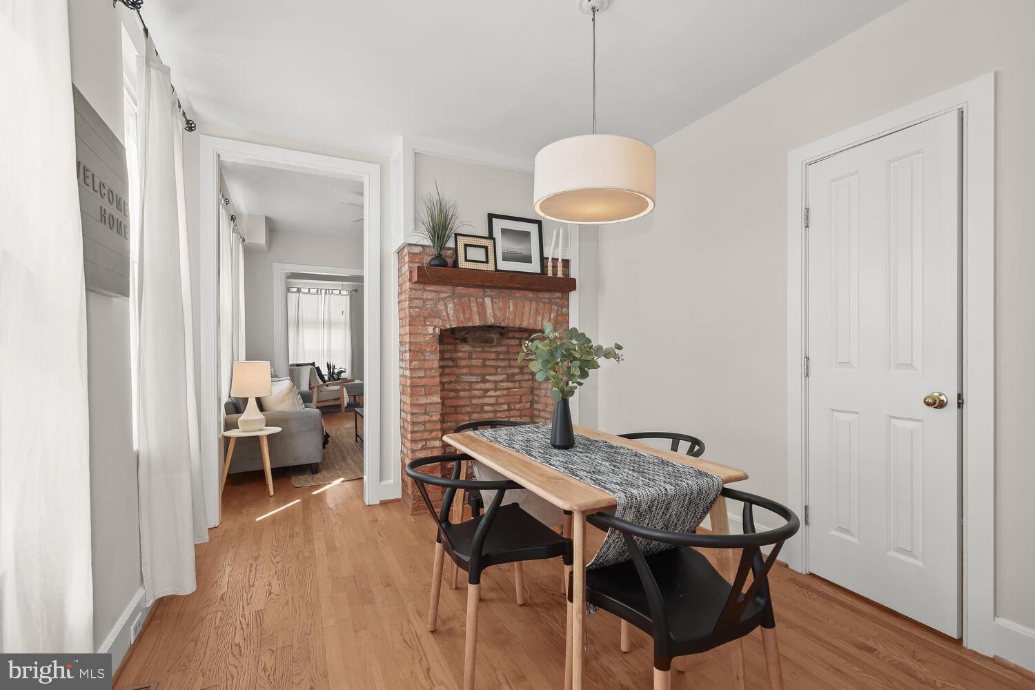 Dining room with a brick fireplace, wooden table, black chairs, and hardwood floors.