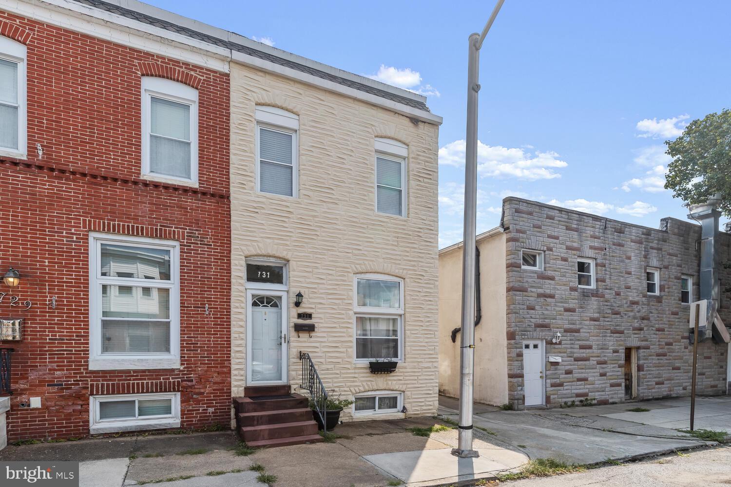 Pale stone-front rowhouse with a white door and dark steps between neighboring Baltimore homes.