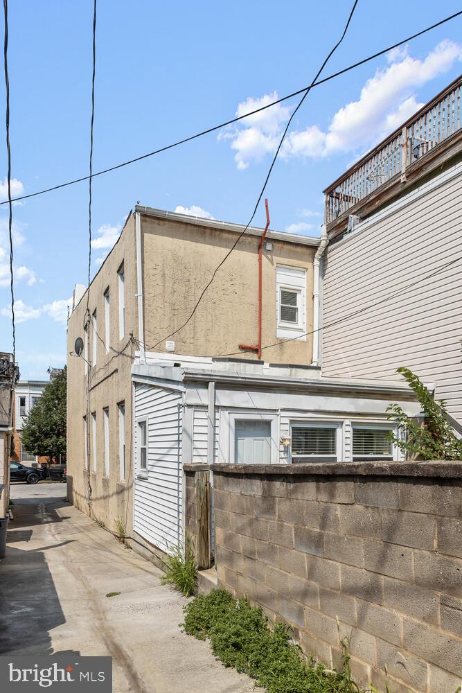 Rear-side of an urban home beside a concrete alley and low block wall.