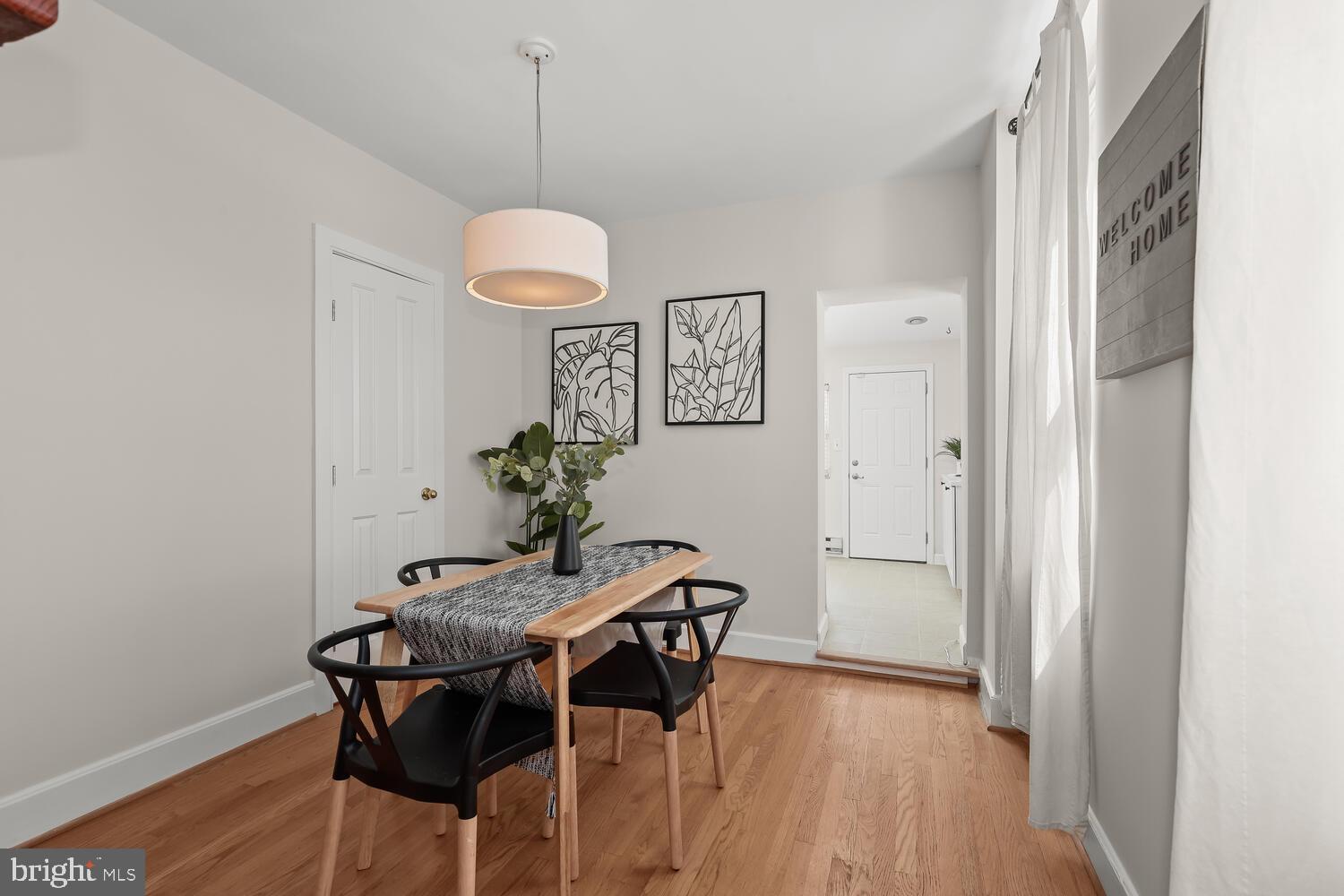 Dining room with a light wood table, black chairs, and botanical wall art beside tall curtained windows.