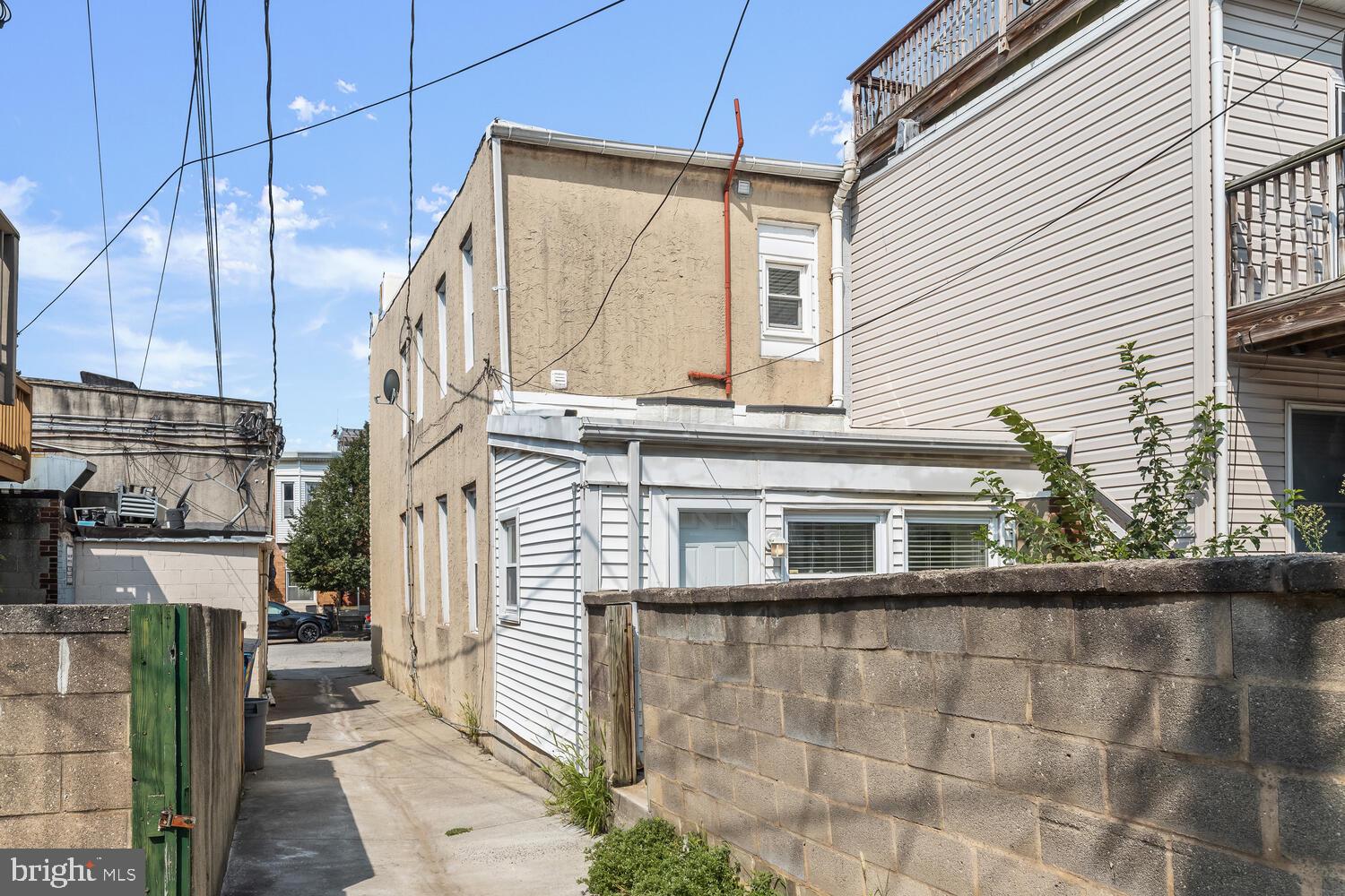 Rear of a building beside a narrow paved alley, with concrete block walls and overhead utility wires.