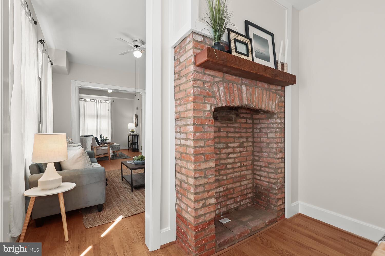 Living room with a large exposed-brick fireplace and a furnished sitting area beyond the doorway.
