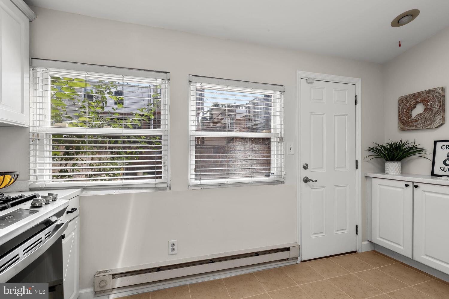 Kitchen with white cabinets, stainless steel range, two windows, and tan tile flooring.