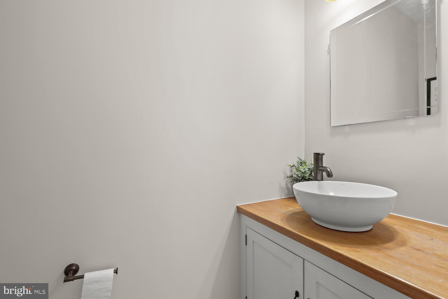 Bathroom vanity with a white vessel sink and warm wood countertop beneath a large mirror.