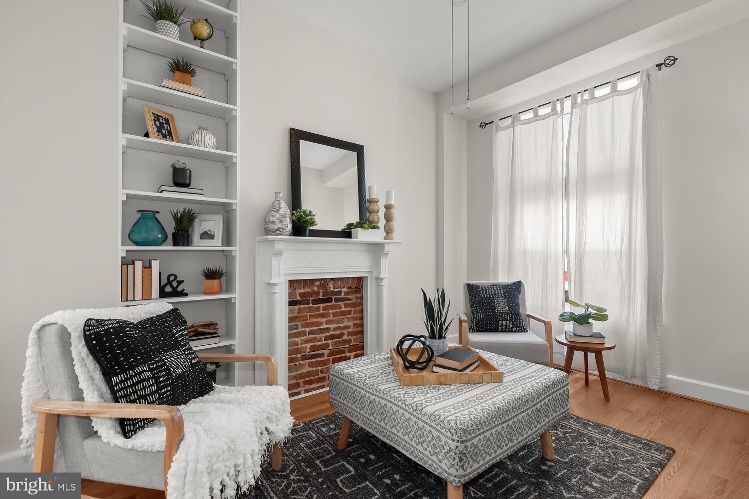 Staged living room with a brick fireplace, built-in shelves, and a patterned ottoman.