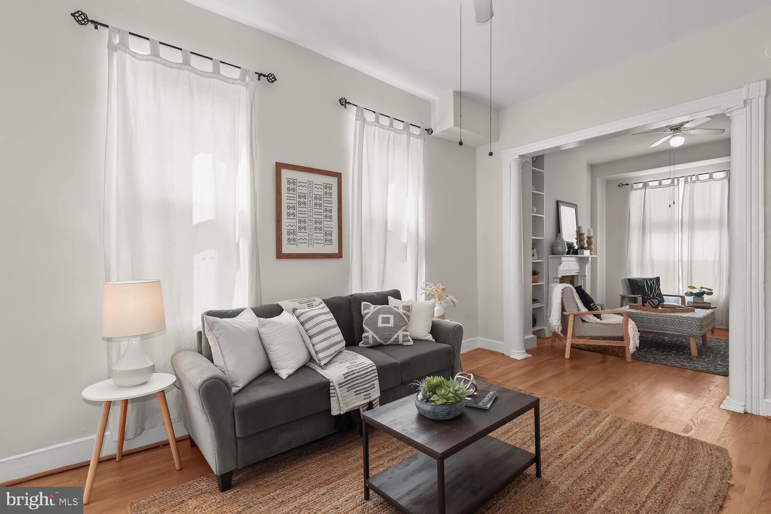 Staged living room with charcoal sofa, tall sheer-curtained windows, and adjoining sitting area.