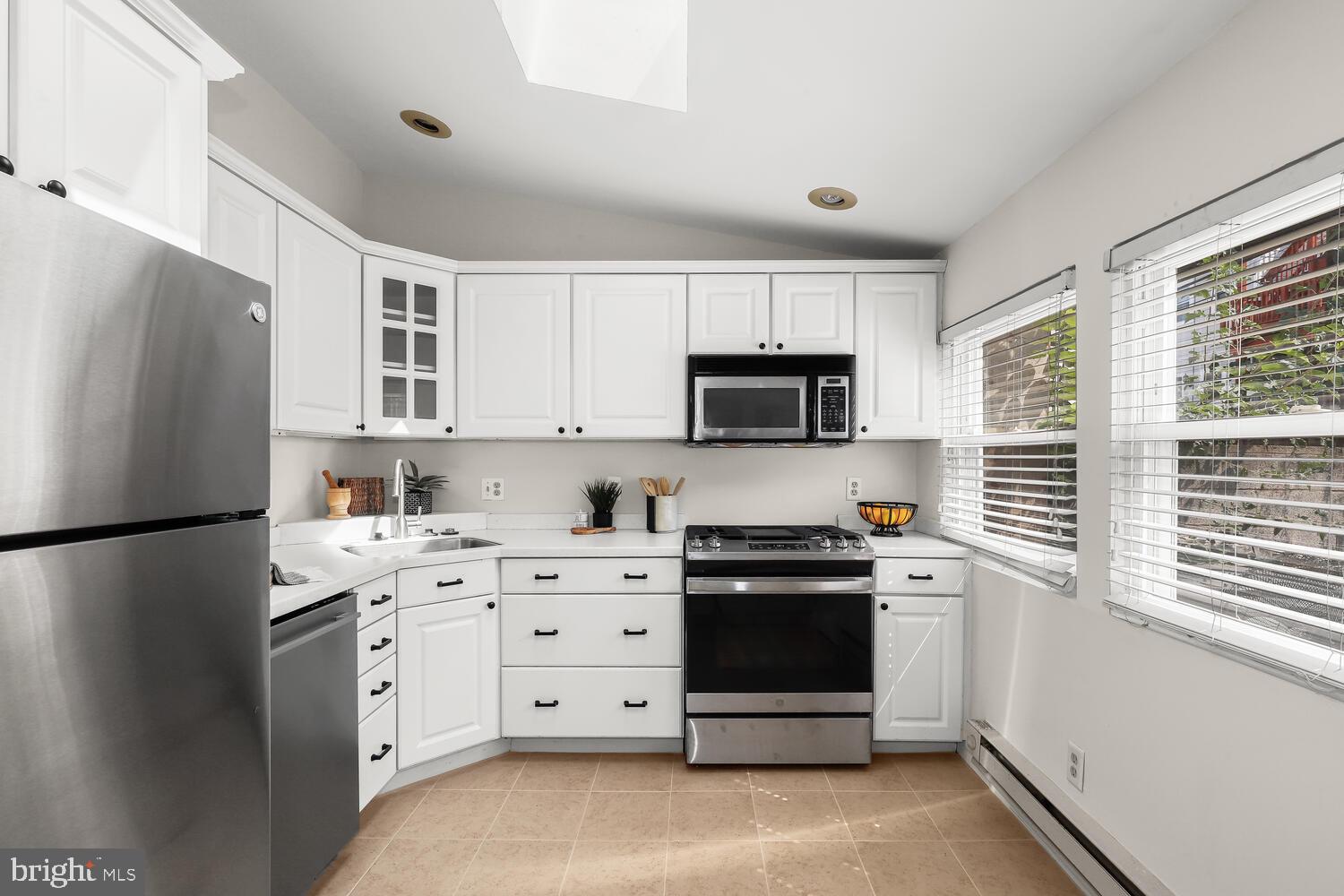 Bright kitchen with white cabinets, stainless steel appliances, and windows with blinds.