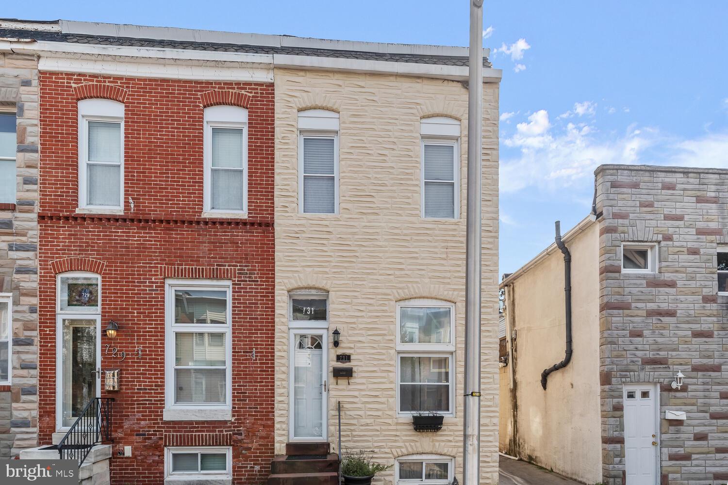 Cream stone Baltimore rowhouse with white-framed windows and a glass front door.