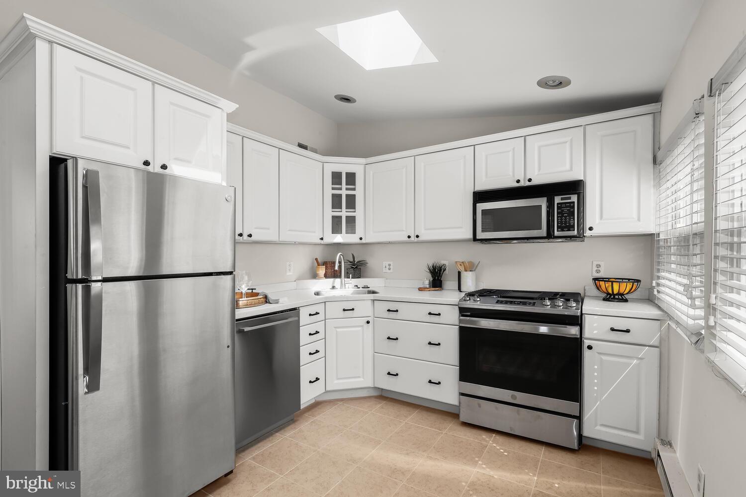 Kitchen with white cabinets, stainless steel appliances, and a window with blinds.