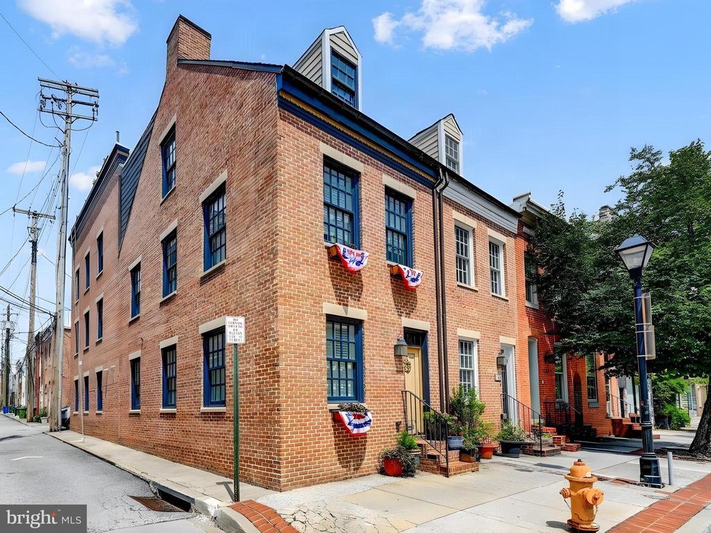 Red-brick row building with dark-framed windows, patriotic bunting, and potted plants by the front steps.