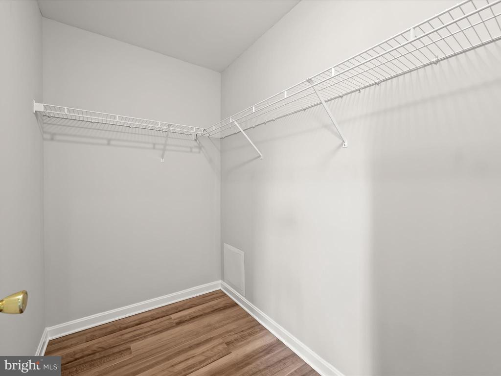 Empty walk-in closet with white wire shelving on two walls and brown wood-look flooring.