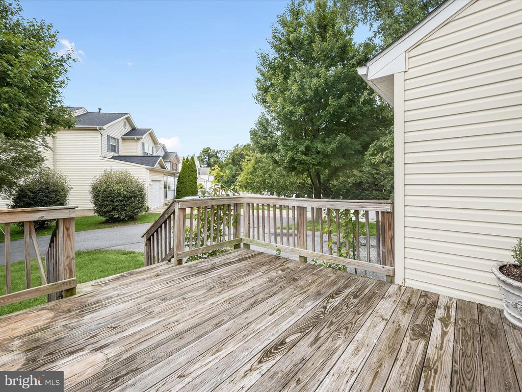Wooden deck beside a light-sided home, with leafy trees and neighboring homes beyond the railing.