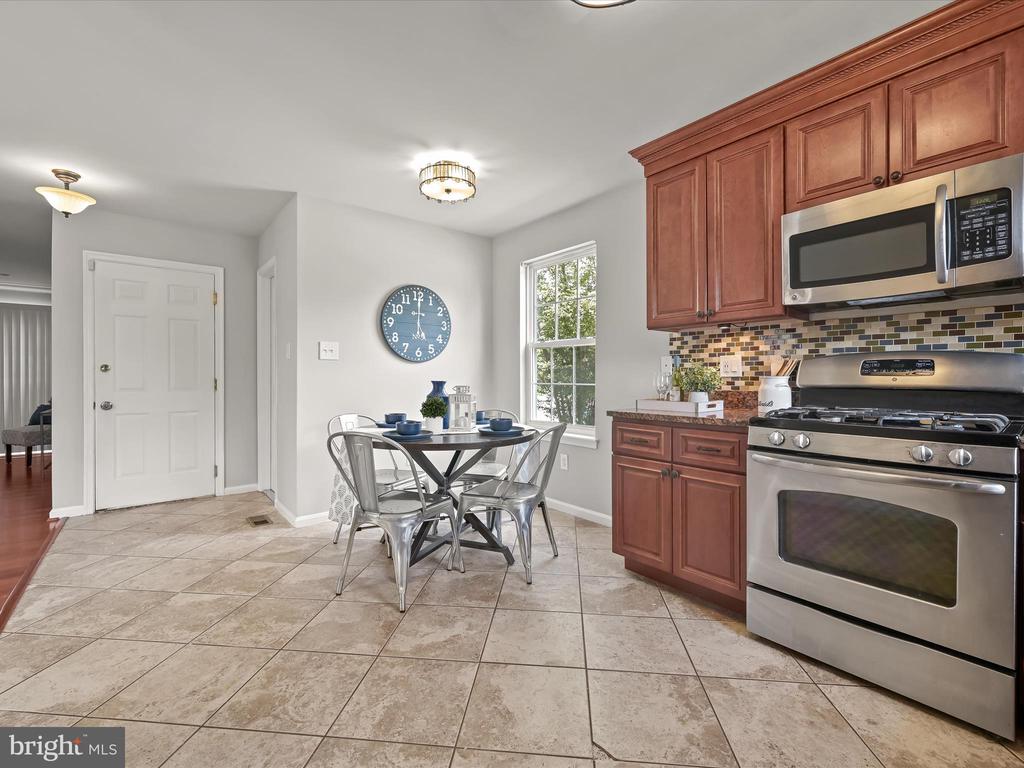 Kitchen and dining area with reddish-brown cabinets, stainless steel appliances, and a round table with metal chairs.
