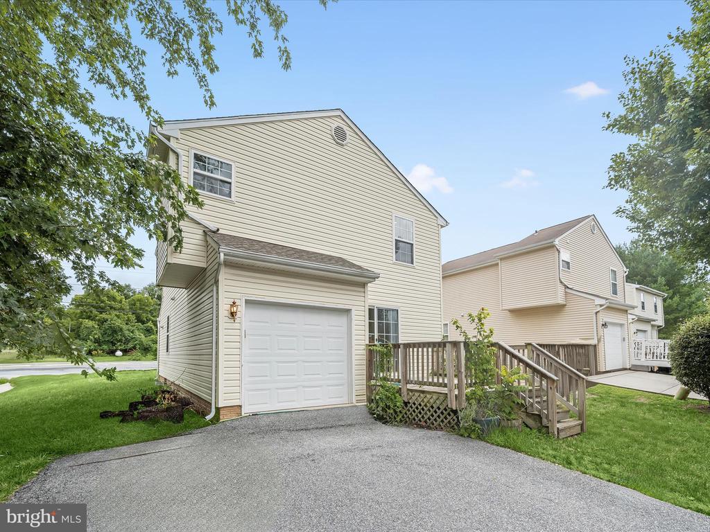 Beige two-story house with an attached garage, curved driveway, and raised wooden deck.