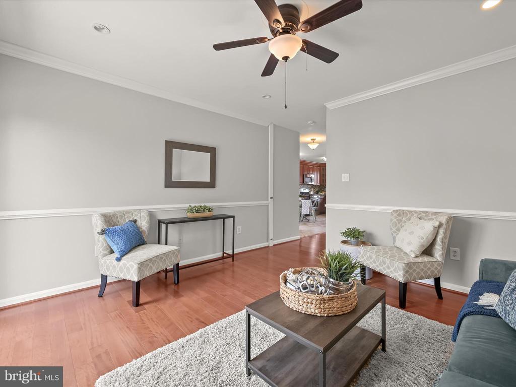 Staged living room with hardwood floors, patterned chairs, and a ceiling fan.