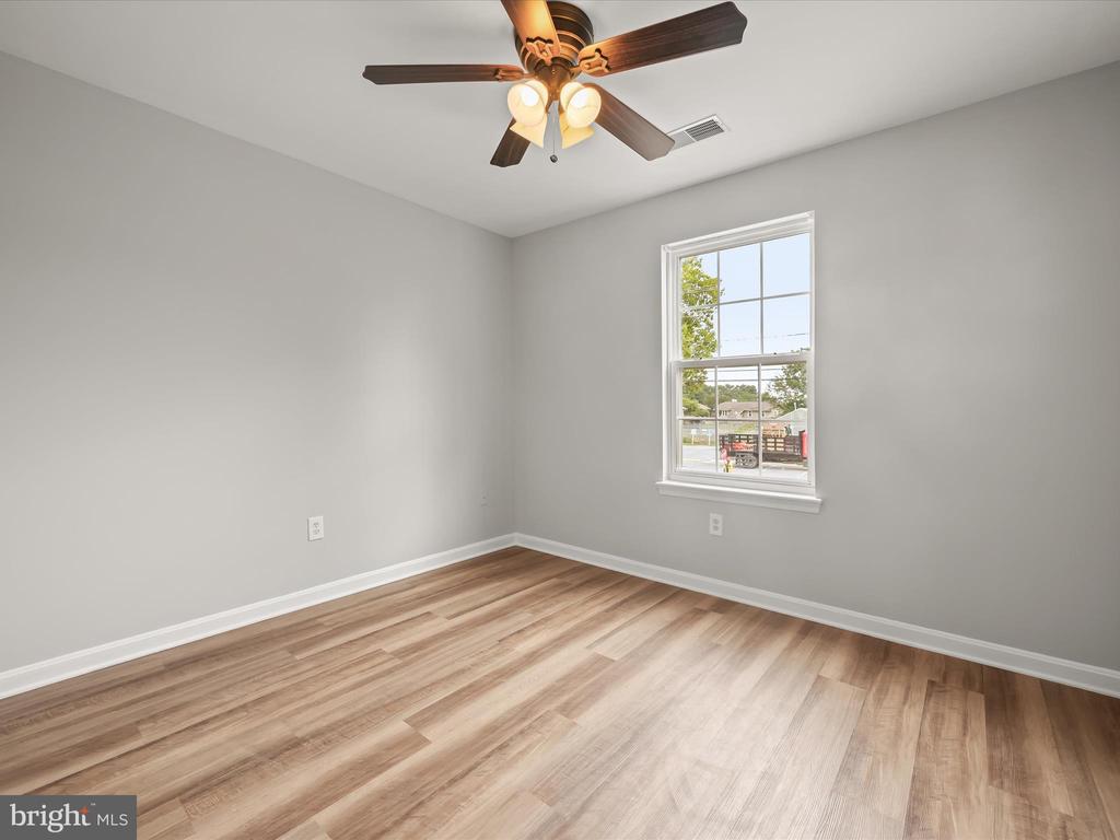 Empty bedroom with wood-look flooring, gray walls, and a window beneath a ceiling fan.