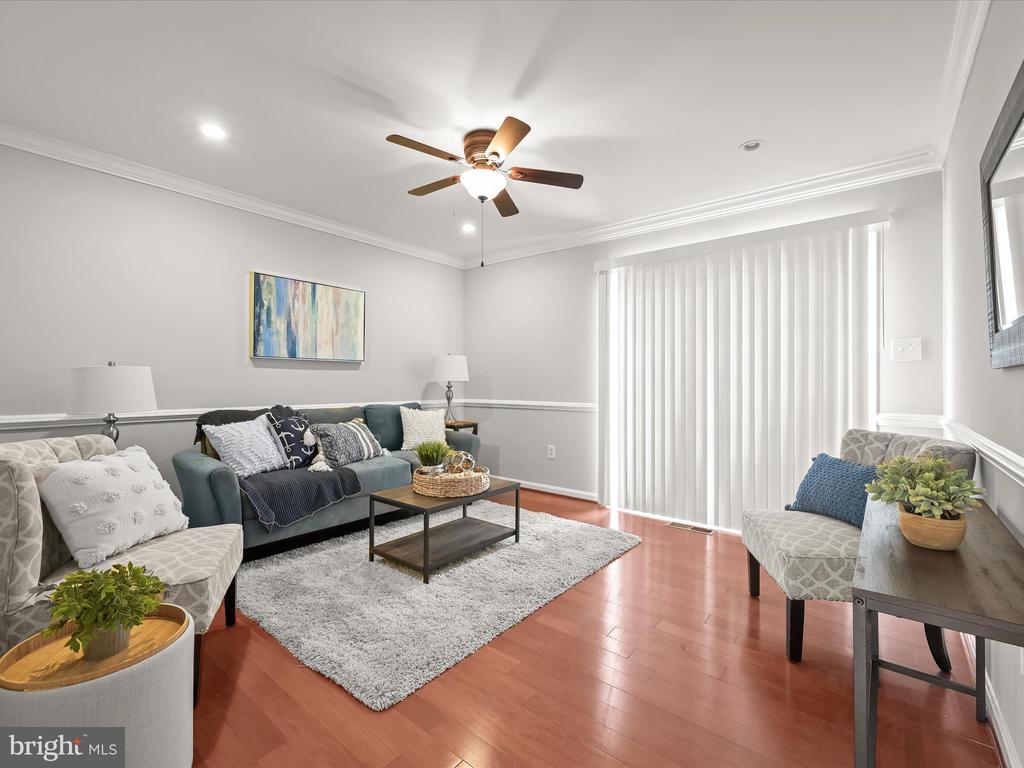 Living room with teal sofa, gray armchairs, hardwood floors, and white vertical blinds.