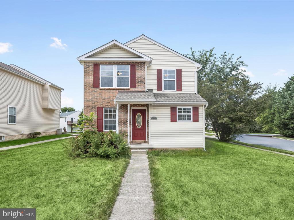 Two-story brick-and-siding home with red shutters, a red front door, and a walkway through the lawn.