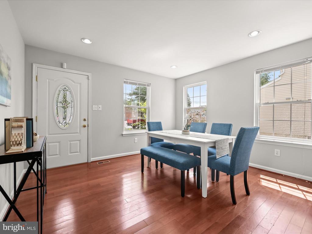 Dining room with blue chairs, a white table, hardwood floors, and a decorative glass front door.