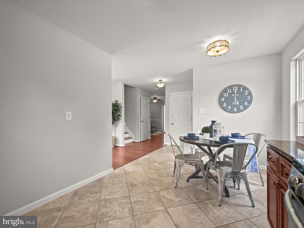 Kitchen dining area with a round table, metal chairs, tiled floor, and large wall clock.