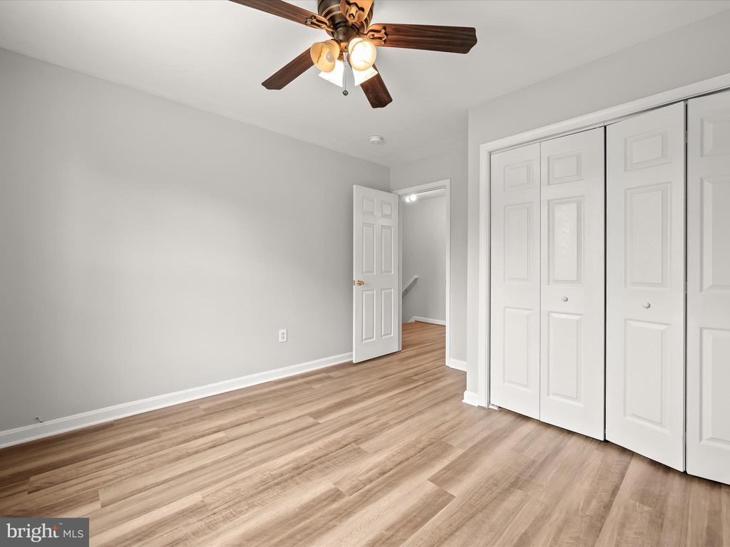 Empty bedroom with wood-look flooring, white closet doors, and a ceiling fan.