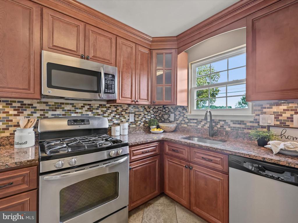Kitchen with reddish-brown cabinets, granite counters, multicolor tile backsplash, and stainless steel appliances.