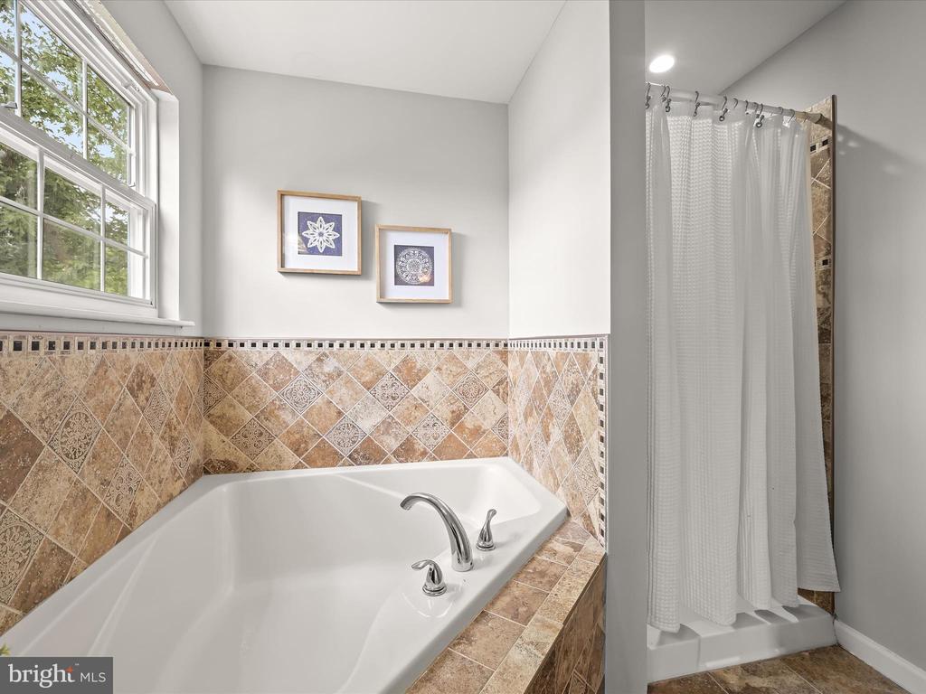 Bathroom with a corner soaking tub, patterned tile surround, and a curtained shower beside a wide window.