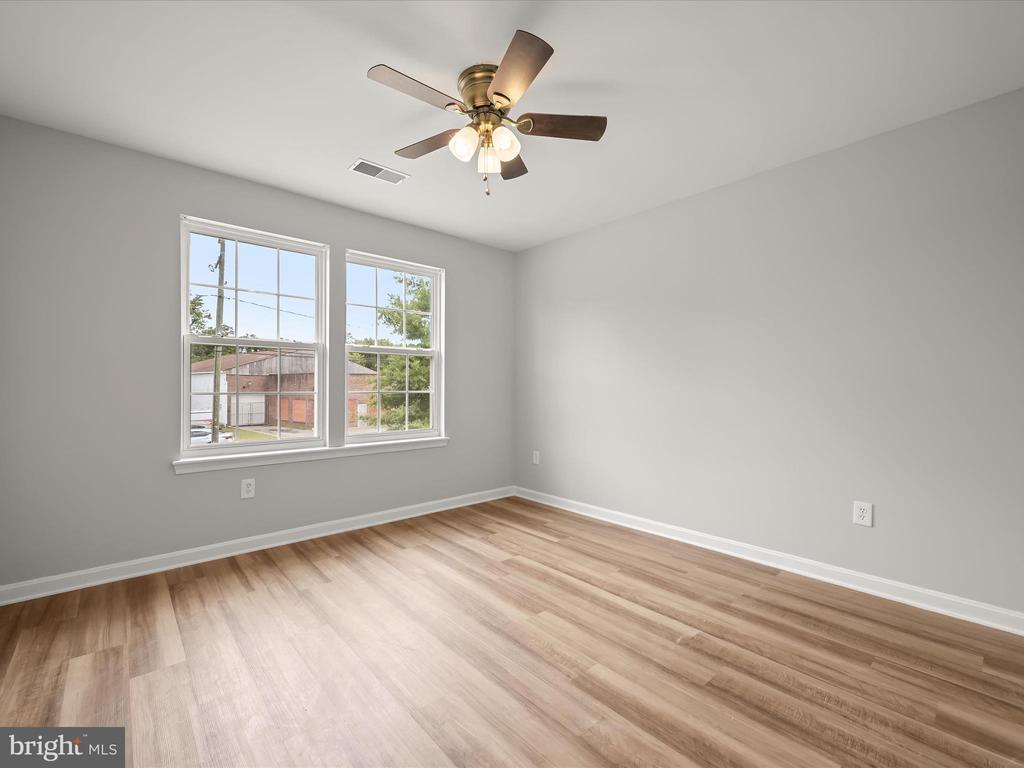 Empty bedroom with wood-look flooring, two windows, and a ceiling fan.