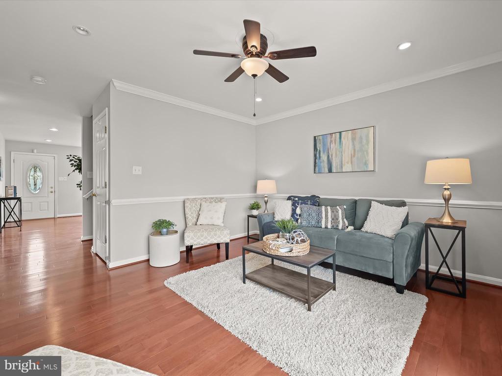 Staged living room with a teal sofa, white area rug, hardwood floors, and ceiling fan.