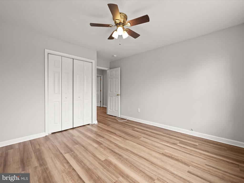 Empty bedroom with wood-look flooring, a white folding-door closet, and a ceiling fan.