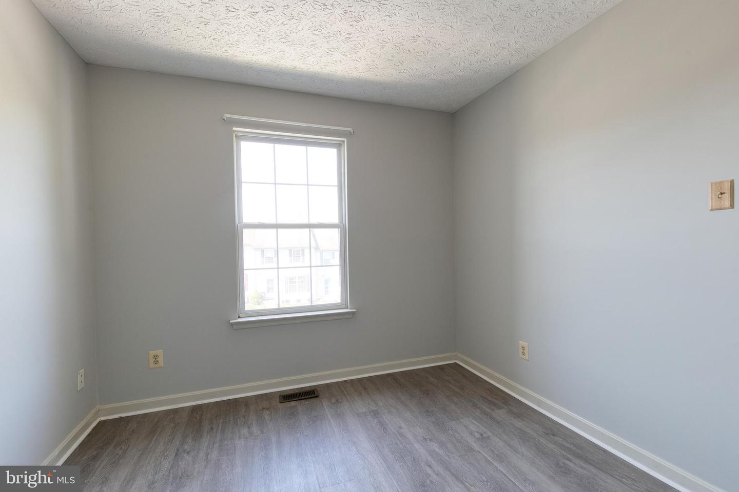 Empty room with gray plank flooring, light gray walls, and a window.